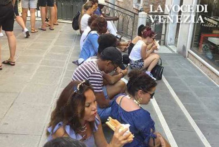 Turisti a Venezia mangiano un panino seduti sul ponte