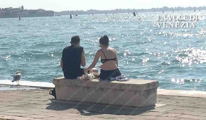 Turisti impegnati in un picnic per strada in Riva Sette Martiri, a Venezia, contemporaneamente la ragazza prende il sole in reggiseno